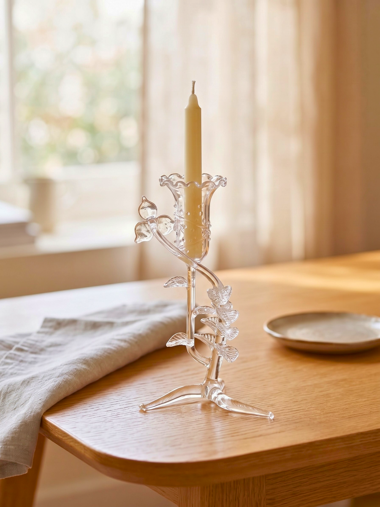 A clear glass candlestick holder with sculptural floral and leaf detail