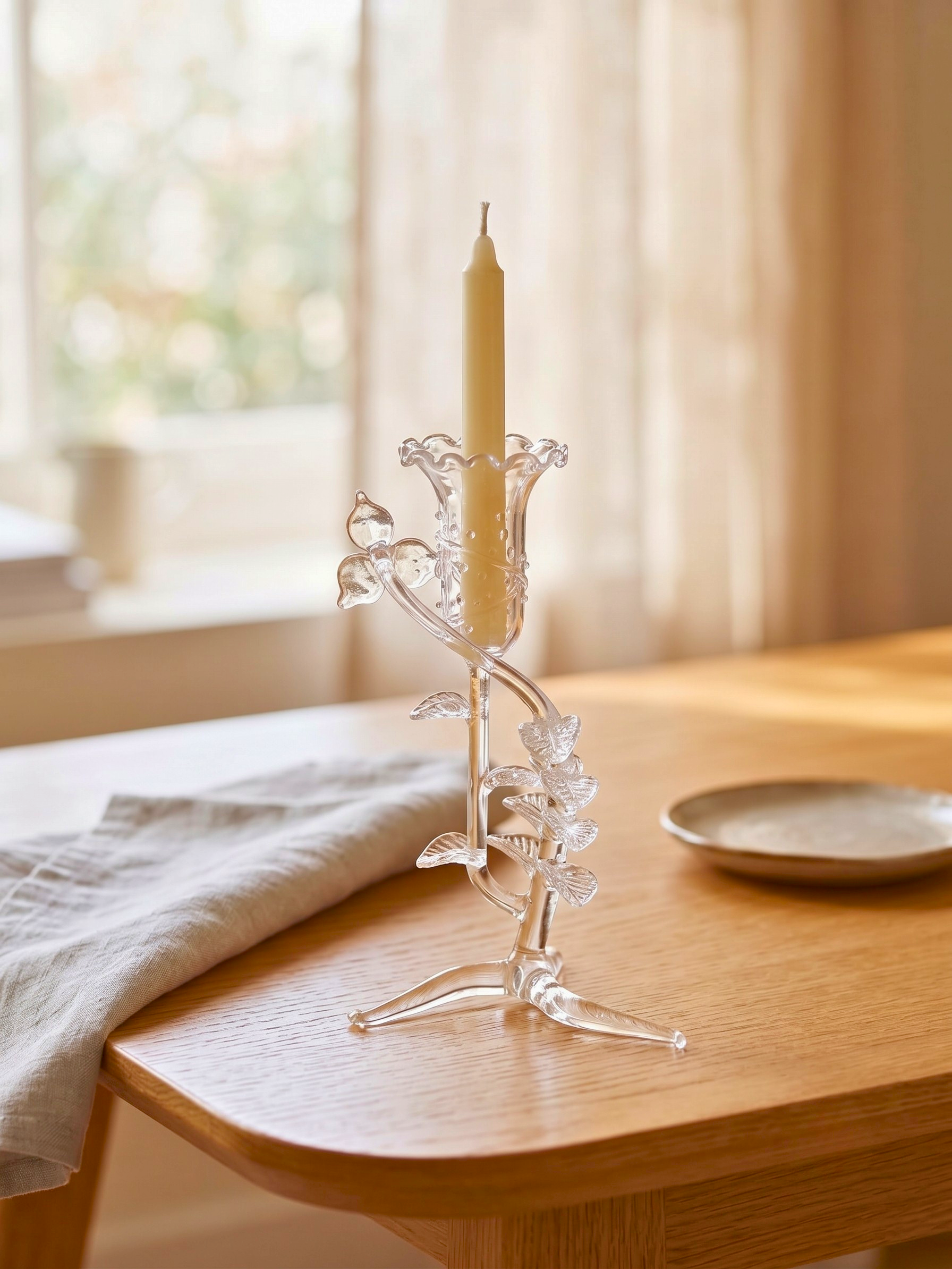 A clear glass candlestick holder with sculptural floral and leaf detail